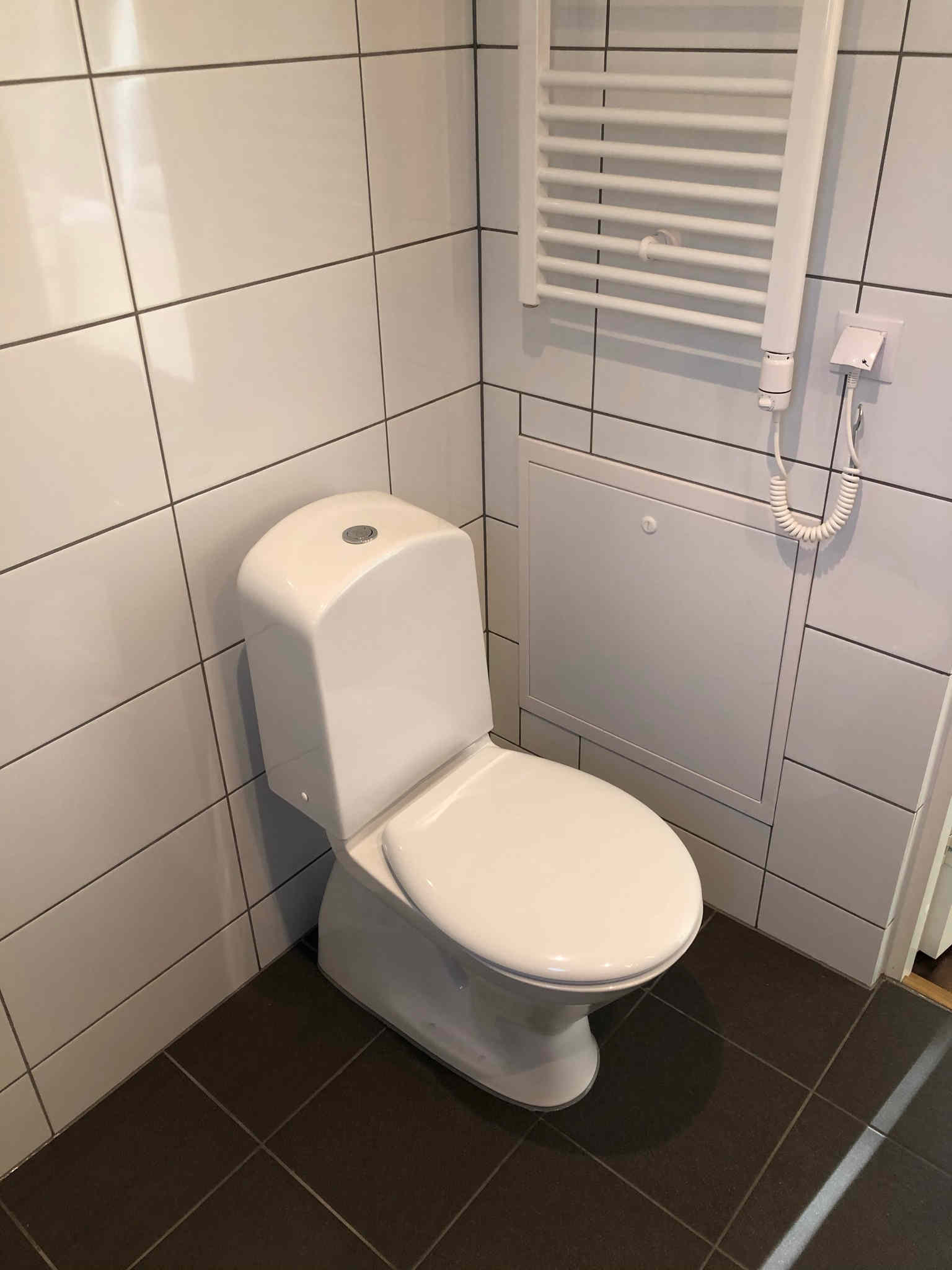 Badrum med plats för tvättmaskin, dusch, toalett, handfat och förvaring.