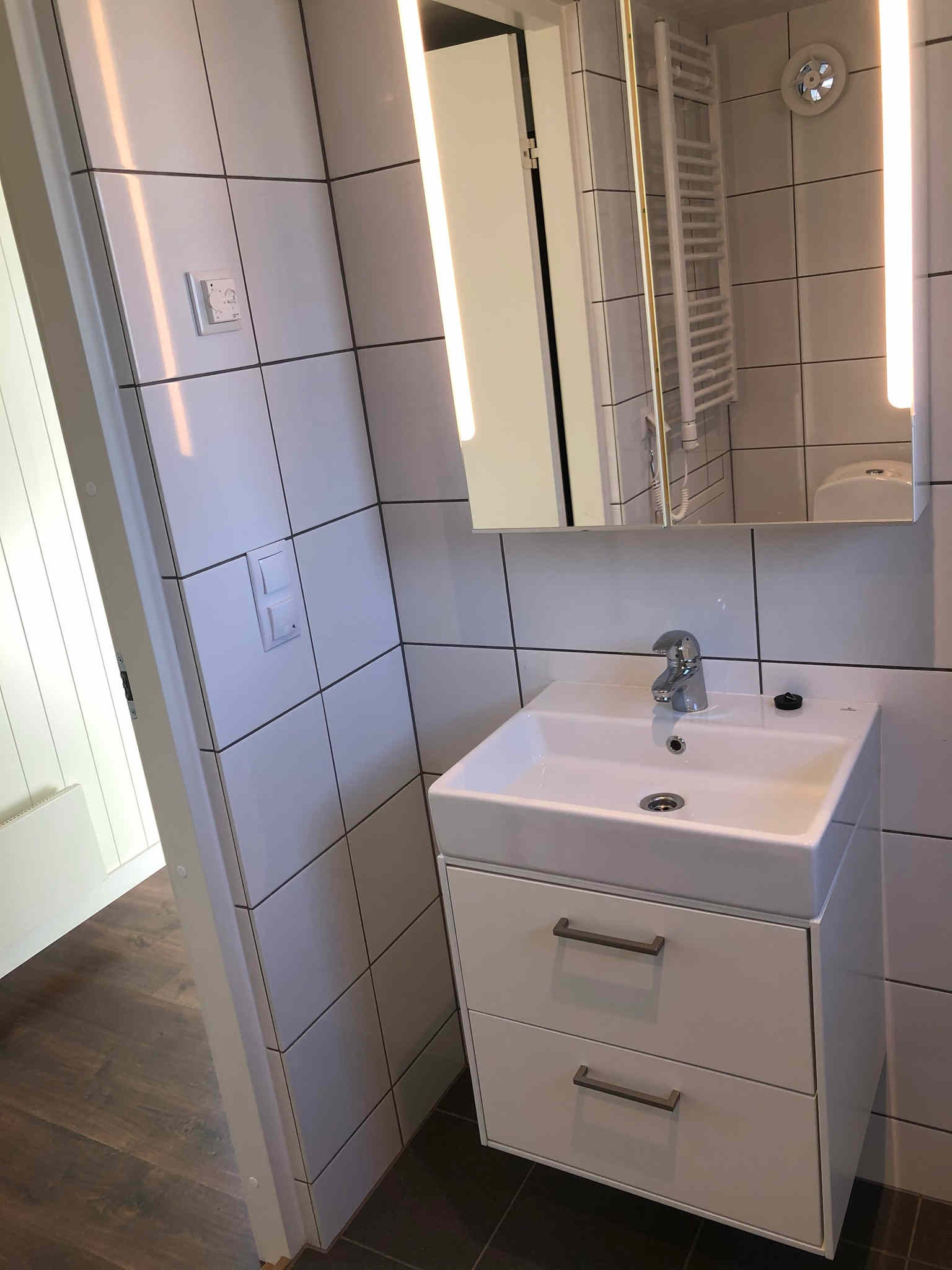 Badrum med plats för tvättmaskin, dusch, toalett, handfat och förvaring.