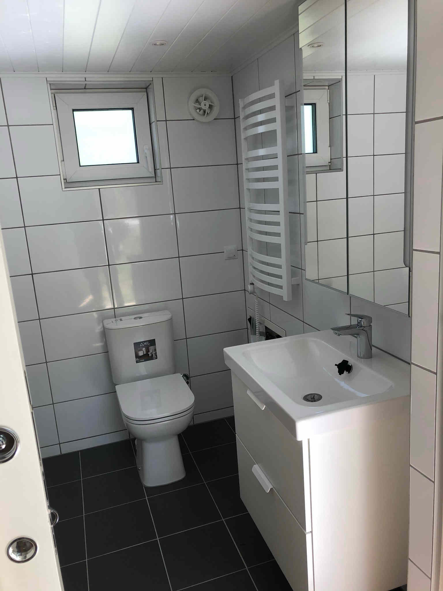 Badrum med plats för tvättmaskin, dusch, toalett, handfat och förvaring.