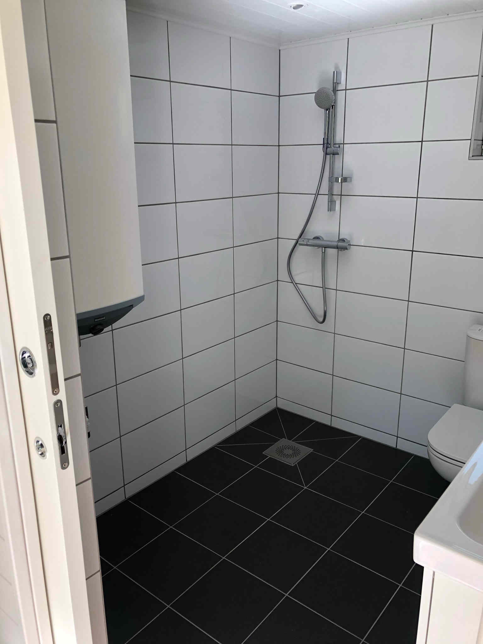 Badrum med plats för tvättmaskin, dusch, toalett, handfat och förvaring.